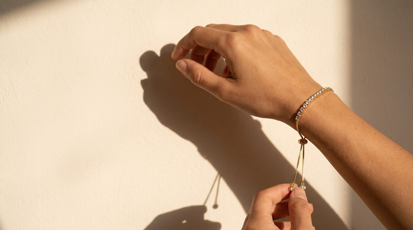 Mano con la Pulsera Cadena en baño de rodio dorado, luz de tarde sobre muro crema